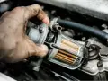 Brudna ręka mechanika trzyma filtr paliwa. Zapchany filtr gazu objawy mogą być różne, np. nierówna praca silnika.
