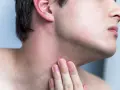 Hombre tocando su cuello con irritación y pequeños granos después de afeitarse.
