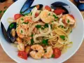 Pyszne linguini z krewetkami, kalmarami i małżami, ozdobione pomidorkami i natką pietruszki.