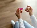 Dłonie trzymające test ciążowy, który wskazuje na 1 miesiąc ciąży.