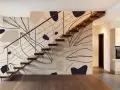 El papel pintado en las paredes de esta casa moderna presenta un diseño abstracto de hojas y formas orgánicas en tonos tierra, complementando la escalera flotante de madera.