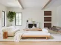 Un elegante salón blanco y madera natural, con sofá curvo, chaise longue, chimenea de mármol y sillas de cuero.