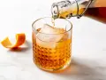 Amaretto co to? Bursztynowy likier z migdałów i moreli, nalewany do szklanki z lodem, z ozdobną skórką pomarańczy.
