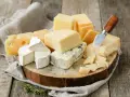 Różnorodne sery ostre gatunki: pleśniowy, żółty z dziurami, brie i parmezan, ułożone na drewnianej desce z gałązką rozmarynu.