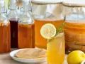 Verre de kombucha rafraîchissant, entouré de bouteilles et de bocaux, rappelant l'origine de cette boisson fermentée.