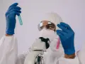 Badacz w kombinezonie i masce analizuje próbki w probówkach, przygotowując się do pracy w laboratorium chemicznym.