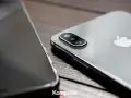 Dwa telefony leżą obok siebie na drewnianym blacie. Jeden z nich, srebrny iPhone, ma widoczny moduł aparatu. Drugi, z ciemnym ekranem, jest ustawiony bokiem. Idealne do rozmowy przez **Facetime**.