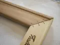 Détail d'un coin de cadre en bois, montrant comment tendre une toile sans châssis avec des agrafes.