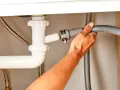 Ręka podłącza wąż odpływowy zmywarki do syfonu pod zlewem. Prosty poradnik, jak podłączyć zmywarkę.