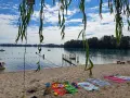 Ein sonniger Tag am Lauterbourg See. Handtücher liegen am Sandstrand, Kinder planschen im Wasser.