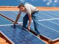 Instalator montuje panele fotowoltaiczne na dachu. Pokazuje, jak zamontować panele fotowoltaiczne, by czerpać energię ze słońca.
