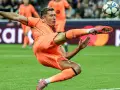 Piłkarz w pomarańczowym stroju wykonuje akrobatyczne kopnięcie do piłki. To Robert Lewandowski, który gra w Lidze Mistrzów.
