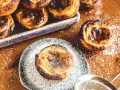 Leckeres Pastel de Nata Rezept: goldbraune Törtchen mit Puderzucker bestäubt, bereit zum Genießen.