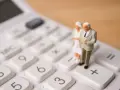 Figurki starszej pary na kalkulatorze symbolizują planowanie przyszłości i obliczanie emerytury stażowej.