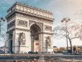 La majestuosa entrada del Arco del Triunfo en París, con esculturas y detalles ornamentales, bajo un cielo azul y árboles otoñales.