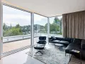 Nowoczesny salon z panoramicznym oknem narożnym, czarną skórzaną kanapą i fotelem Eames. Widok na zielone wzgórza.