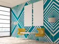 Modern room with striking **diseños pared geometrica** in teal and white. Two yellow chairs and a table sit before the wall, with floor lamps and blank canvases.