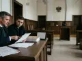 Prawnik w todze omawia dokumenty z klientem w sali sądowej. Czy do apelacji potrzebny jest adwokat? Tak, często jest niezbędny.