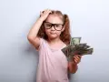 Mała dziewczynka w okularach trzyma plik banknotów, zastanawiając się nad zaskórniakami i innymi dziwadłami z krainy portfela.