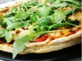 Pyszna pizza z rukolą, pomidorami i serem, pachnąca ziołami. Idealna na szybki obiad.