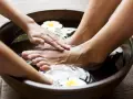 Soaking feet in a warm bath with Epsom salt for feet infection. A hand gently massages the foot, surrounded by water and white flowers.