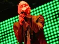 Wokalista REM, Michael Stipe, śpiewa na scenie, gdy światła migoczą na zielono.