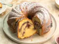 Ein Gugelhupf mit Marmelade, bestäubt mit Puderzucker. Ein Stück ist bereits angeschnitten und zeigt die köstliche Füllung.