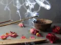 Humo de incienso de lavanda asciende, evocando paz y el significado espiritual de la calma. Pétalos secos y un cuenco completan la escena.