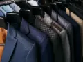 Różne rodzaje marynarek męskich wiszą na wieszakach: granatowa w drobną kratkę, szara w kratę, z brązowymi łatami na łokciach i beżowa.