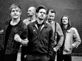 Fünf Männer stehen vor einer gemusterten Wand. Sie sehen aus wie eine energiegeladene Punkband, bereit, die Bühne zu rocken.