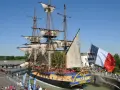 Le majestueux bateau l'Hermione, réplique d'une frégate du XVIIIe siècle, est amarré, pavoisé du drapeau français. Une foule s'est rassemblée pour admirer ce navire historique.