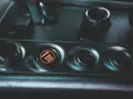 Podświetlany przycisk "ENGINE START STOP" w samochodzie. Obok niego pokrętło wyboru trybu jazdy, jak czujnik IBS.