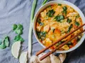 Miseczka z tajską zupą curry z kurczakiem, makaronem ryżowym i warzywami, podana z pałeczkami.