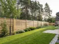 En vacker trädgård med en modern träribbstaket som ramar in gräsmattan och buskar.