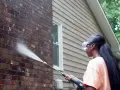 Woman pressure washing a dark acid wash brick wall, restoring its natural beauty.