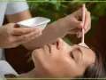 Kosmetyczka aplikuje na czoło klientki peeling z kwasami AHA za pomocą pędzelka.