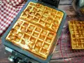 Frisch gebackene belgische Waffeln in einer Waffelform, daneben eine auf einem Rost.