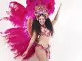 Uśmiechnięta tancerka w barwnym stroju z piórami, wykonująca samba krok podstawowy.