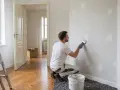 Mann spachtelt Wandlöcher, um den Mietvertrag bei Auszug zu erfüllen. Leiter und Farbeimer stehen bereit.