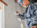 Elektryk w kasku i okularach pracuje przy instalacji. Sprawdź nasz cennik usług budowlanych, by poznać koszty remontu.