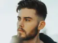 Ein Mann mit Bart und einem modernen taper fade design im Haar blickt nachdenklich zur Seite.
