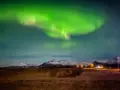 Islandia pogoda luty: zielona zorza polarna nad ośnieżonymi górami i polami.