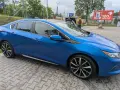 Błękitny Chevrolet Volt z czarnym dachem, zaparkowany na mokrej kostce brukowej. W tle widać stację KFC.