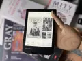 Drewniana dłoń wskazuje na ekran czytnika PocketBook, gdzie wyświetla się okładka książki Stephena Kinga "Później". W tle widać inne książki.