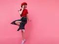 Dziewczyna w czerwonym beretce i sukience w grochy, w stylu pin up, skacze na różowym tle.
