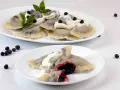 Pyszne pierogi z jagodami, polane śmietaną i ozdobione miętą. Na talerzu widać też kilka świeżych jagód.