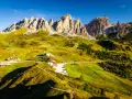 Panorami mozzafiato sull'**Alta Via numero 2 Dolomiti**. Sentieri serpeggianti tra prati verdi e imponenti vette rocciose sotto un cielo azzurro.