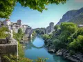 Widok na Mostar w Bośni z kamiennym mostem Stary Most nad turkusową rzeką Neretwą. W tle kamienne budynki i góry.
