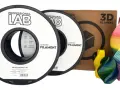 Dwie szpule filamentu jaki filament PLA marki Professional Lab, obok pudełka z napisem "3D FILAMENT" i kolorowych wydruków 3D.