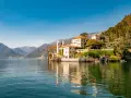 A scenic journey from Milan to Lake Como reveals this stunning villa on the water's edge, with mountains in the distance.